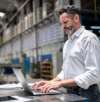Mann arbeitet mit Laptop in einer industriellen Produktionshalle.