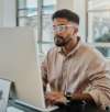 Mann mit Brille arbeitet an einem Desktop-Computer in einer hellen Büroumgebung.