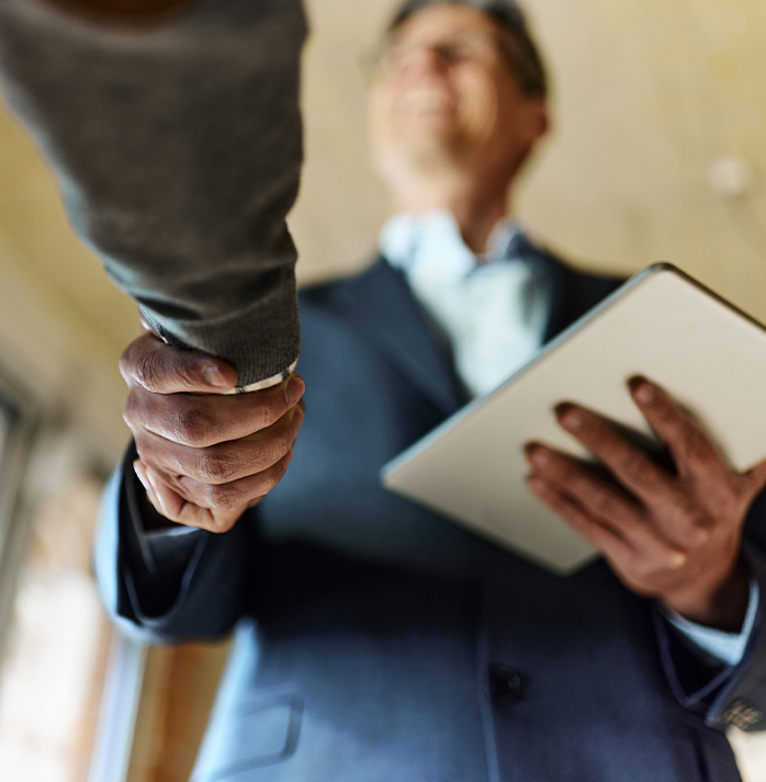 A businessman in a suit shaking hands with another person, holding a tablet, symbolizing a successful business agreement